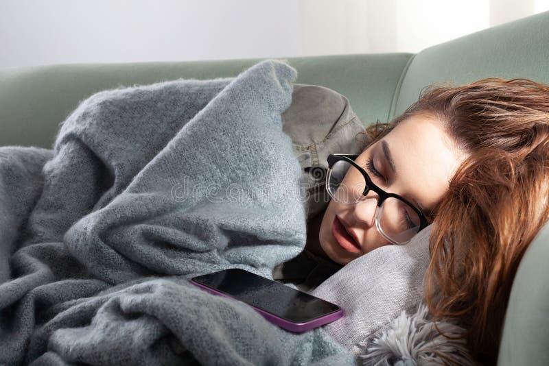 Den unga kvinnan som är utmattad av smartphone-slingor på soffan med sin telefon. Begreppet överdriven användning av sociala medie royaltyfri foto