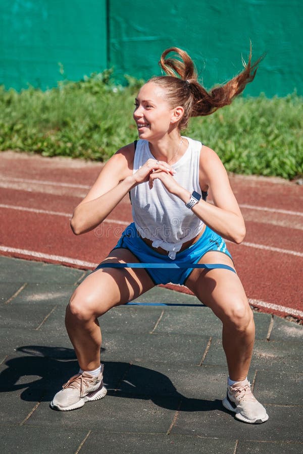 Den unga kvinnan utför höjdhoppövningar med en konditionresårmusikband på hennes fot på sportjordning fotografering för bildbyråer Den unga kvinnan utför höjdhoppövningar med en konditionresårmusikband på hennes fot på sportjordning fotografering för bildbyråer