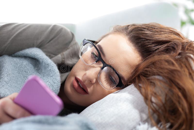 Den unga kvinnan är utmattad av smartphone-beroende som ligger på soffan när hon tittar på telefonskärmen. Begreppet överdrivna so arkivbilder