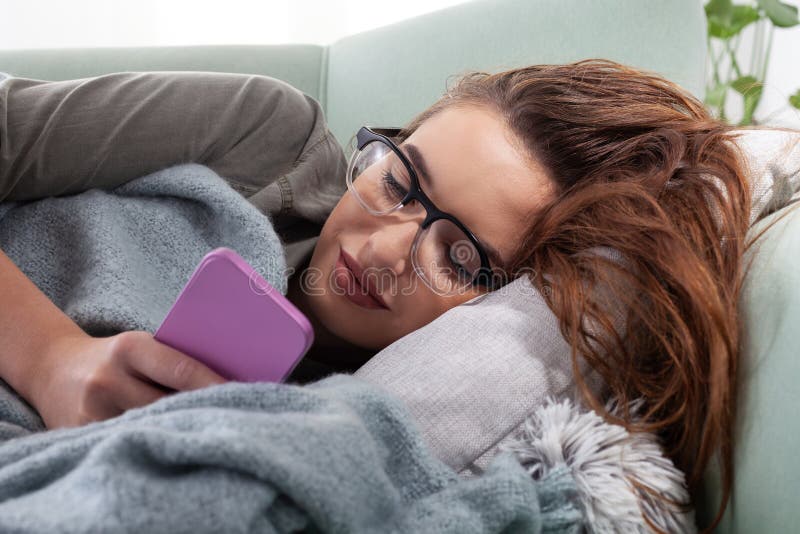 Den unga kvinnan är utmattad av smartphone-beroende som ligger på soffan när hon tittar på telefonskärmen. Begreppet överdrivna so royaltyfri fotografi