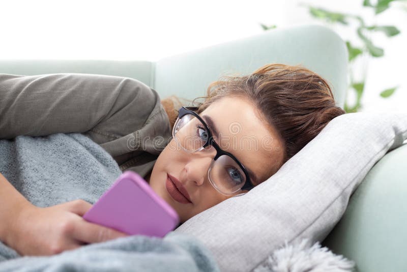 Den unga kvinnan är utmattad av smartphone-beroende som ligger på soffan när hon tittar på telefonskärmen. Begreppet överdrivna so royaltyfri foto