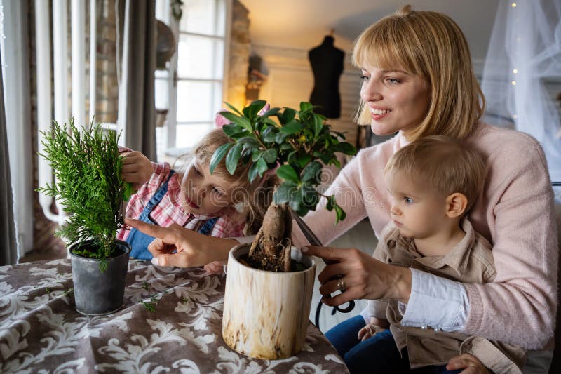 Den unga lyckliga kvinnan med sina små barn planterar och vattnar husväxter hemma. royaltyfri foto