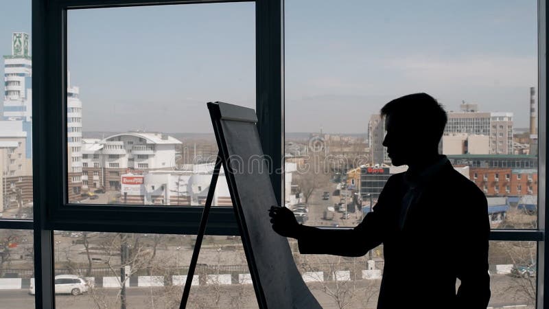 Den unga mannen skriver på whiteboardanseende på fönsterbakgrund i modern inre