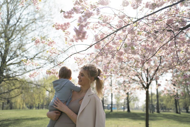 Den unga modermamman som rymmer hennes litet, behandla som ett barn sonpojkebarnet under att blomstra SAKURA Cherry tr?d med fall fotografering för bildbyråer Den unga modermamman som rymmer hennes litet, behandla som ett barn sonpojkebarnet under att blomstra SAKURA Cherry tr?d med fall fotografering för bildbyråer
