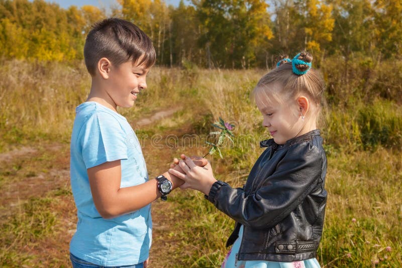 Den unga pojken ger en flicka blommor på naturen i höst royaltyfria foton Den unga pojken ger en flicka blommor på naturen i höst royaltyfria foton