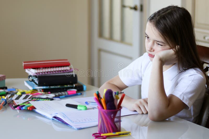 Den unga skolflickan är uppriven och trött av att göra skolaläxa arkivfoto Den unga skolflickan är uppriven och trött av att göra skolaläxa arkivfoto