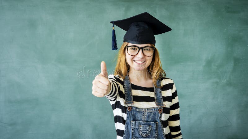 Den unga studentflickavisningen tummar upp på den gröna svart tavlan royaltyfri bild Den unga studentflickavisningen tummar upp på den gröna svart tavlan royaltyfri bild