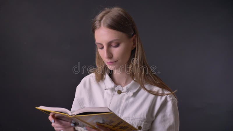 Den unga söta flickan är läseboken som håller ögonen på på kameran, grå bakgrund