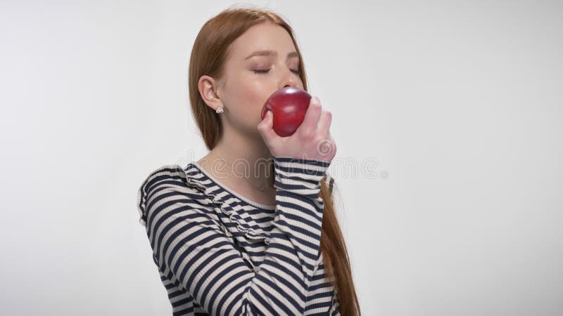 Den unga söta ljust rödbrun flickan är det stickande röda äpplet som tycker om det, vit bakgrund
