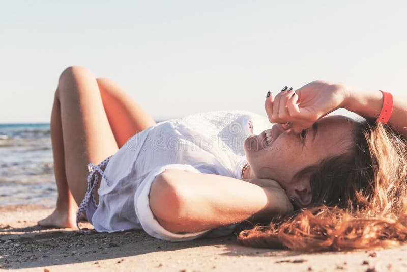 Den unga vuxna brunbrända blonda flickan ligger på sanden på stranden nära arkivfoto Den unga vuxna brunbrända blonda flickan ligger på sanden på stranden nära arkivfoto