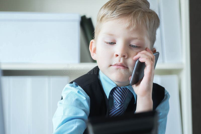 Den unge företagaren som har förtroende och chef på kontoret pratar i telefonen och sitter vid skrivbordet med en bärbar dator royaltyfri bild