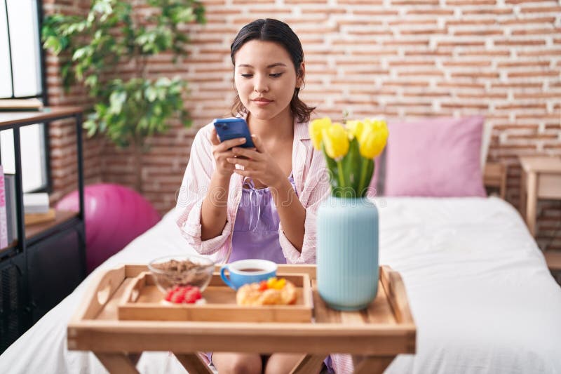 Den unge hispanikkvinnan gör foto med smartphone för att ge frukost i sovrummet fotografering för bildbyråer