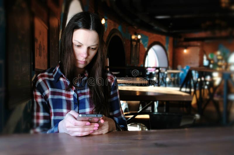 Den upprivna kvinnan överför ett meddelande i telefonsammanträdet i ett kafé Iklätt en plädskjorta royaltyfri fotografi Den upprivna kvinnan överför ett meddelande i telefonsammanträdet i ett kafé Iklätt en plädskjorta royaltyfri fotografi