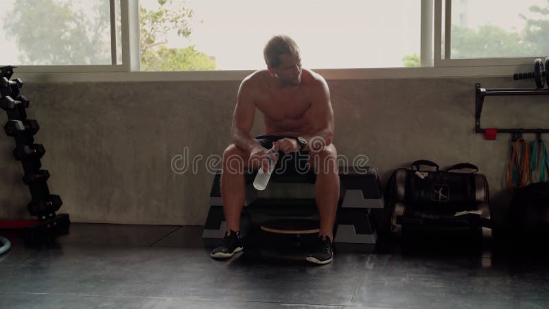 Den vackra kroppsformen hos en stilig ung man som tränar i ett fitness-centrum. Han är trött och dricker vatten på gymmet lager videofilmer