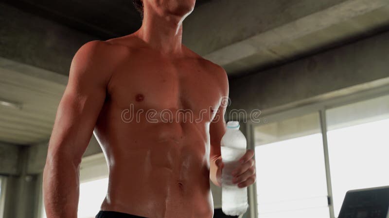 Den vackra kroppsformen hos en stilig ung man som tränar på ett fitness-center när han dricker vatten. lager videofilmer