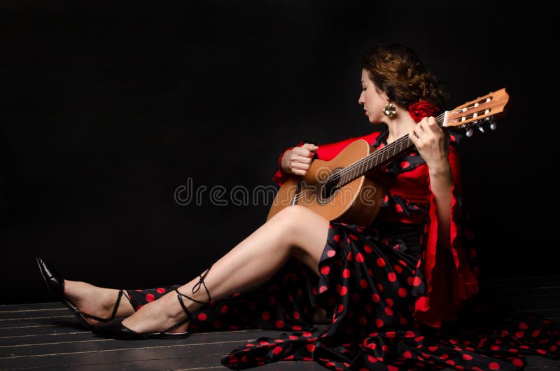 Den vackra kvinnan i röd klänning med gitarr på mörk bakgrund på golvet