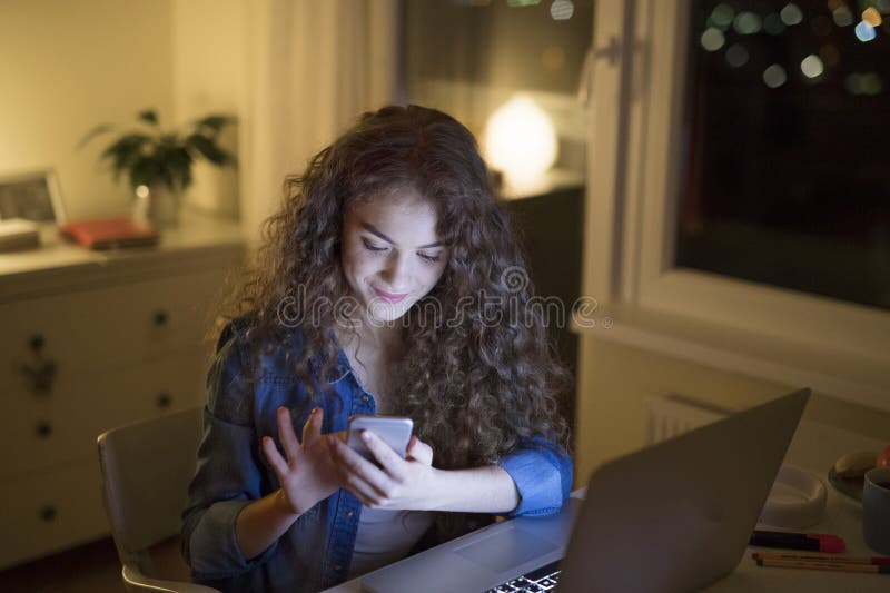 Den vackra universitetsstudenten skriver sin teori på en bärbar dator som sitter hemma på bordet och rullar på royaltyfri fotografi