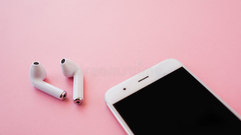 Den vita trådlösa hörlurar och smartphonen ligger på en ljus rosa bakgrund Hörlurar ut ur laddande fall royaltyfri fotografi Den vita trådlösa hörlurar och smartphonen ligger på en ljus rosa bakgrund Hörlurar ut ur laddande fall royaltyfri fotografi