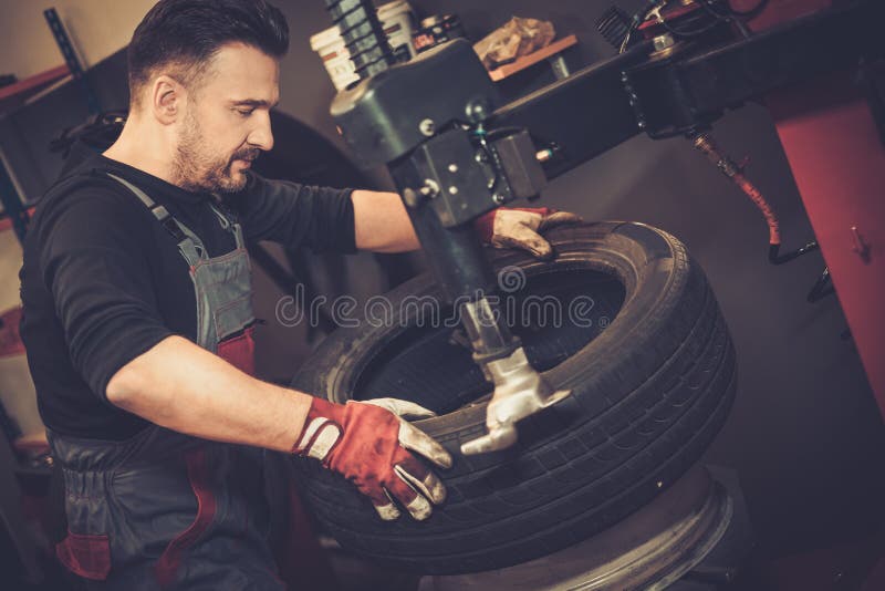 Professional car mechanic replace tire on wheel in auto repair service. Professional car mechanic replace tire on wheel in auto repair service.