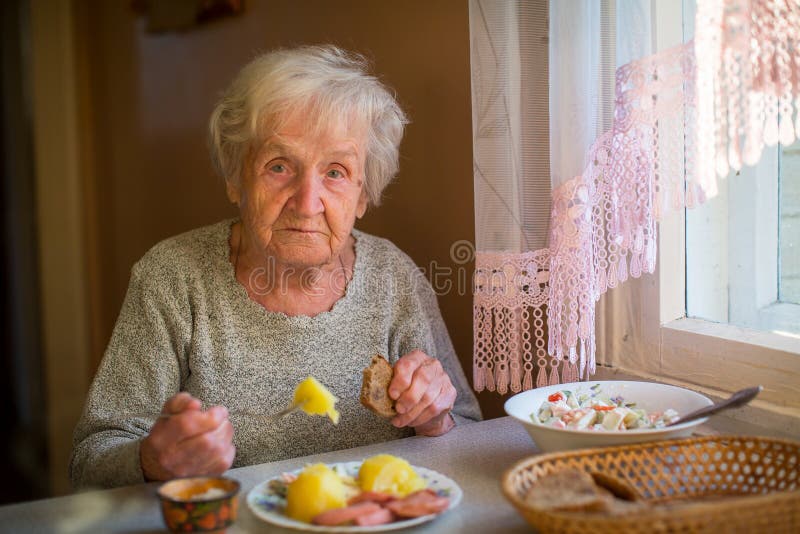Den äldre kvinnan har matställesammanträde på tabellen bara fotografering för bildbyråer Den äldre kvinnan har matställesammanträde på tabellen bara fotografering för bildbyråer