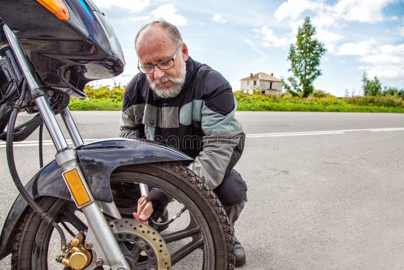 Den äldre mannen kontrollerar hans hjul för motorcykel` s royaltyfri fotografi Den äldre mannen kontrollerar hans hjul för motorcykel` s royaltyfri fotografi
