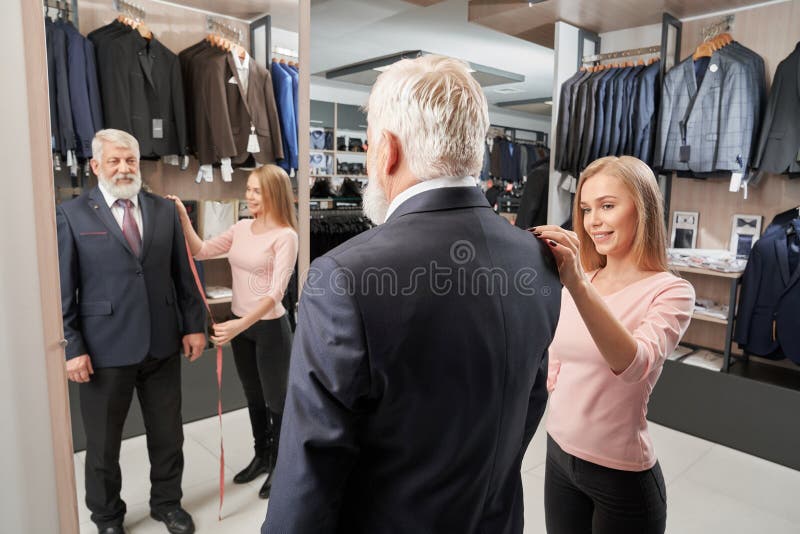 Den äldre mannen som försöker på formell dräkt i kläder, shoppar royaltyfri bild Den äldre mannen som försöker på formell dräkt i kläder, shoppar royaltyfri bild