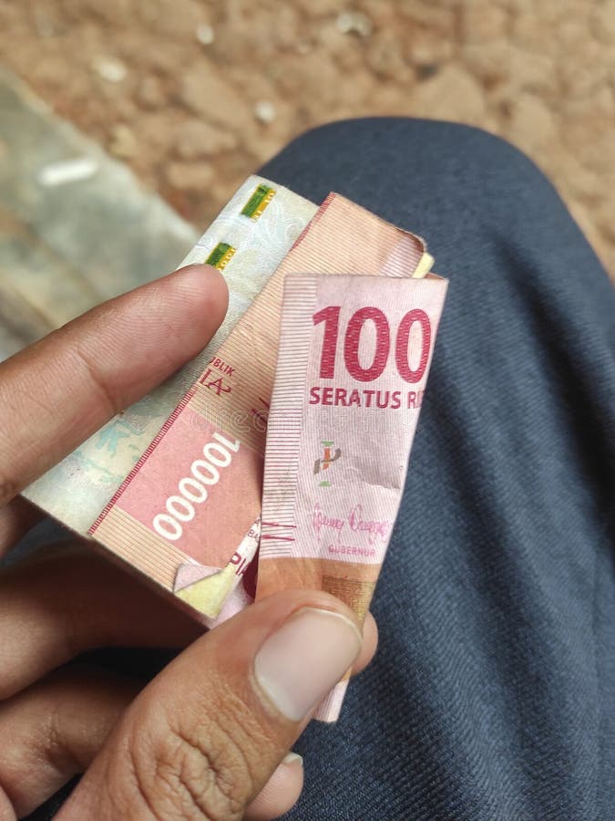 Indonesian state money with a nominal value of one hundred thousand rupiah, in a man& x27;s hand. Indonesian state money with a nominal value of one hundred thousand rupiah, in a man& x27;s hand