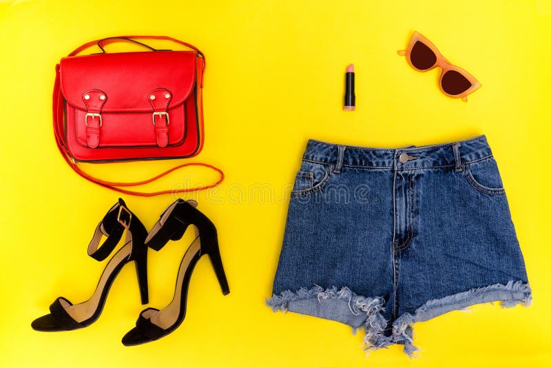 Denim shorts, black shoes, red handbag and glasses. Bright yellow background. Fashionable concept