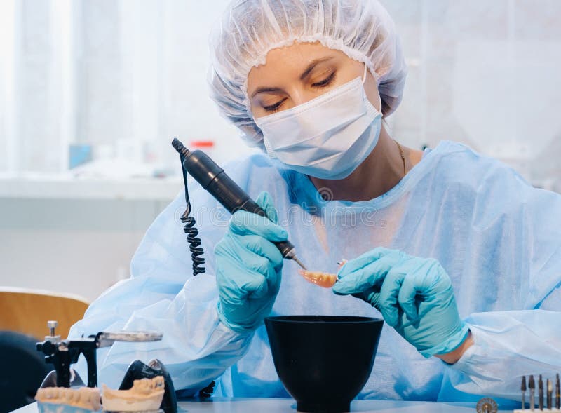A Dental Technician in Protective Clothing is Working on a Prosthetic Tooth in His Laboratory