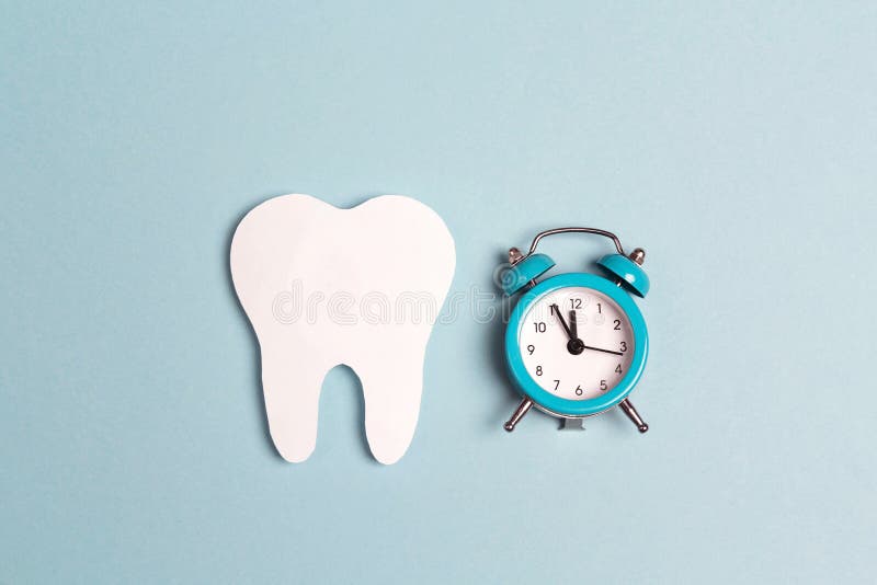 Dente di Libro Bianco con la sveglia su fondo blu Tempo a salute dentaria Disposizione piana, vista superiore, spazio della copia