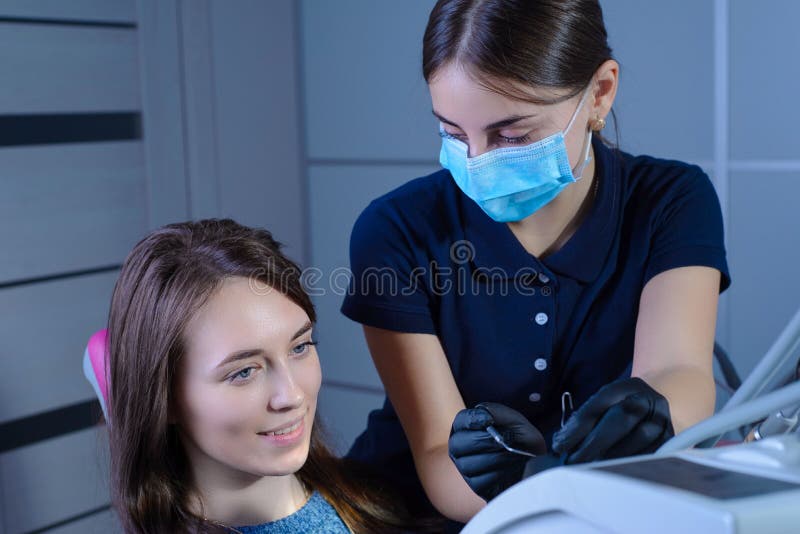 A Dentist in a Mask and Gloves, Shows a Happy Patient an Xray of the Teeth, Telling Her about