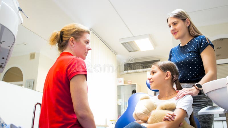 Pediatric dentist talking with girls and her mother in clinic