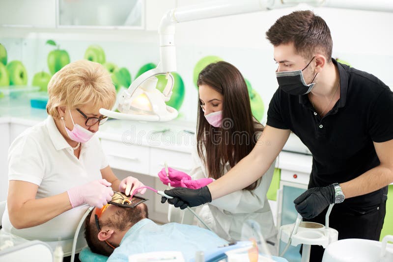 Dentist works with patient, she is assisted by two assistants stock photos Dentist works with patient, she is assisted by two assistants stock photos