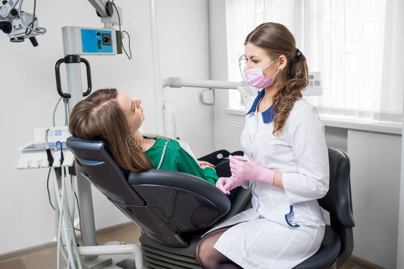 Dentista de sexo femenino joven con el paciente hermoso de la mujer antes del procedimiento dental en oficina dental moderna odon imagen de archivo Dentista de sexo femenino joven con el paciente hermoso de la mujer antes del procedimiento dental en oficina dental moderna odon imagen de archivo