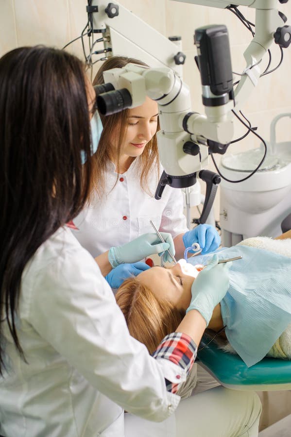 Dentista femminile che tratta la carie facendo uso del microscopio all'ufficio del dentista immagini stock Dentista femminile che tratta la carie facendo uso del microscopio all'ufficio del dentista immagini stock