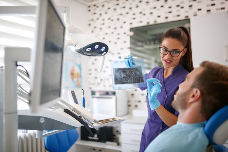 Dentista fêmea que mostra a metragem dental do raio X ao paciente