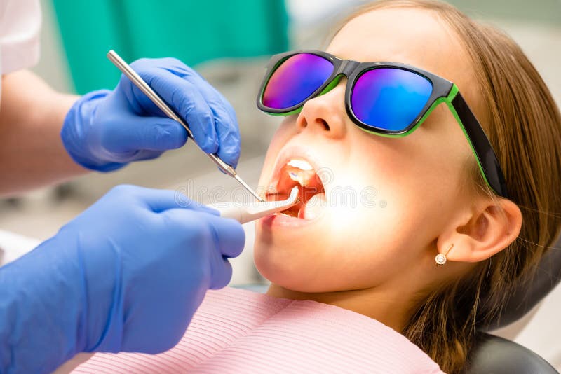 Dentista que examina los dientes elementales de las muchachas de la edad con las herramientas dentales en clínica dental pediát foto de archivo Dentista que examina los dientes elementales de las muchachas de la edad con las herramientas dentales en clínica dental pediát foto de archivo