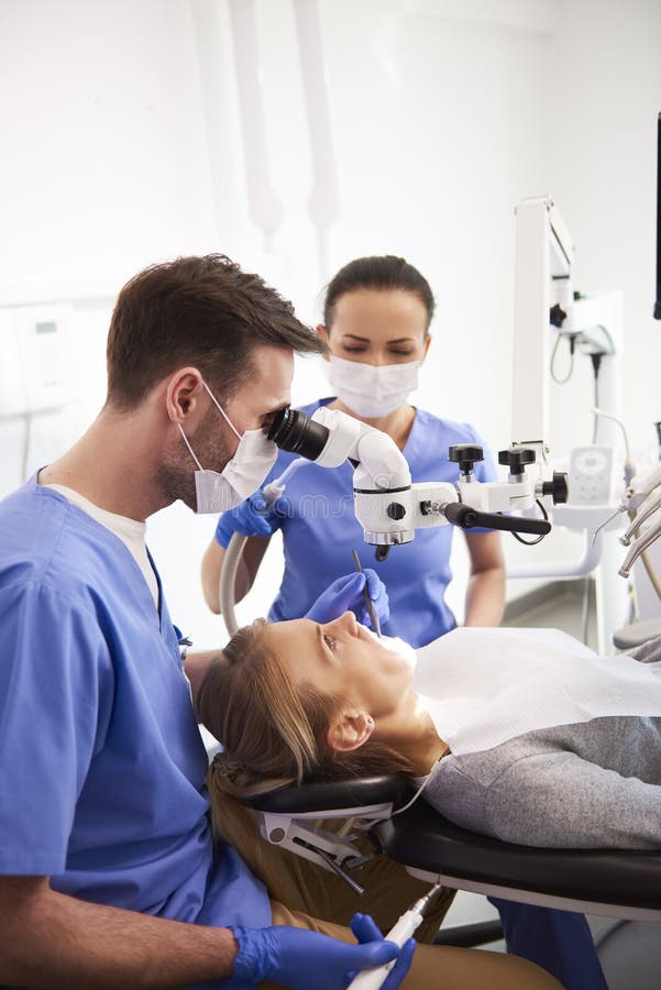 Dentista y su funcionamiento auxiliar con el microscopio dental imágenes de archivo libres de regalías Dentista y su funcionamiento auxiliar con el microscopio dental imágenes de archivo libres de regalías