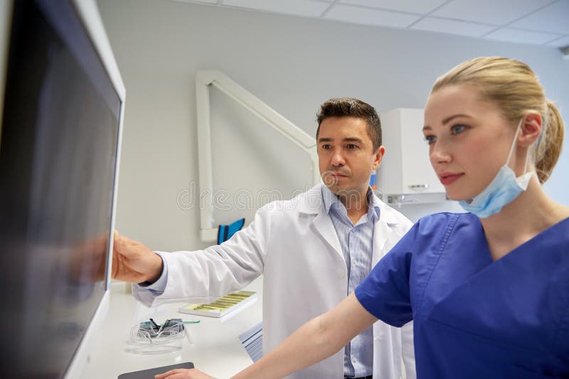 People, medicine, stomatology, technology and health care concept - dentists looking to x-ray scan on monitor at dental clinic. People, medicine, stomatology, technology and health care concept - dentists looking to x-ray scan on monitor at dental clinic