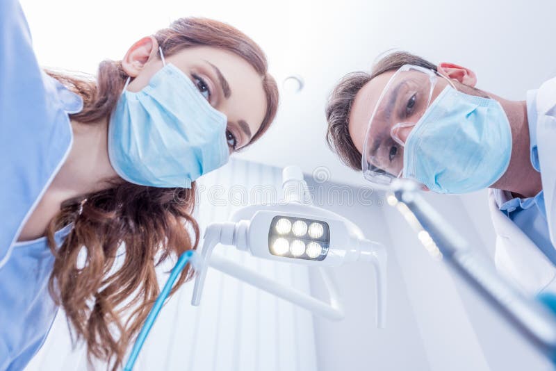 Bottom view of dentists in protective masks holding dental equipment in dentist office. Bottom view of dentists in protective masks holding dental equipment in dentist office