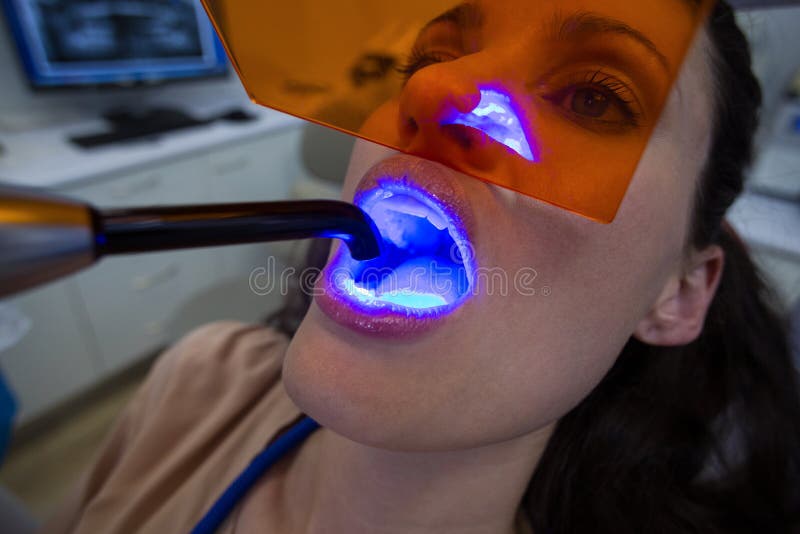 Dentists examining female patient with dental curing light in clinic. Dentists examining female patient with dental curing light in clinic