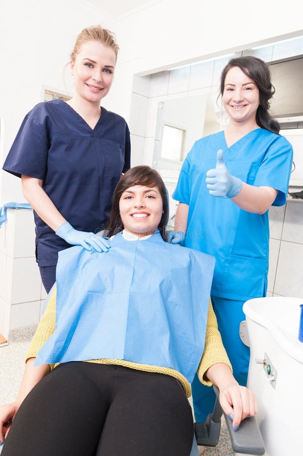 Dentiste amical avec le patient de sourire et le thum de représentation auxiliaire photographie stock Dentiste amical avec le patient de sourire et le thum de représentation auxiliaire photographie stock