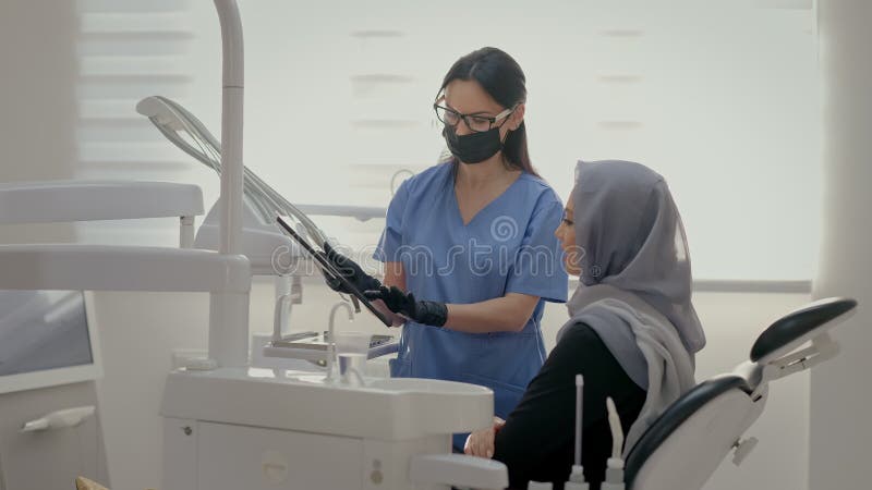 Dentiste travaillant au bureau. visage du jeune patient proche. jeune fille en foulard sur la tête assise sur le fauteuil des dent banque de vidéos