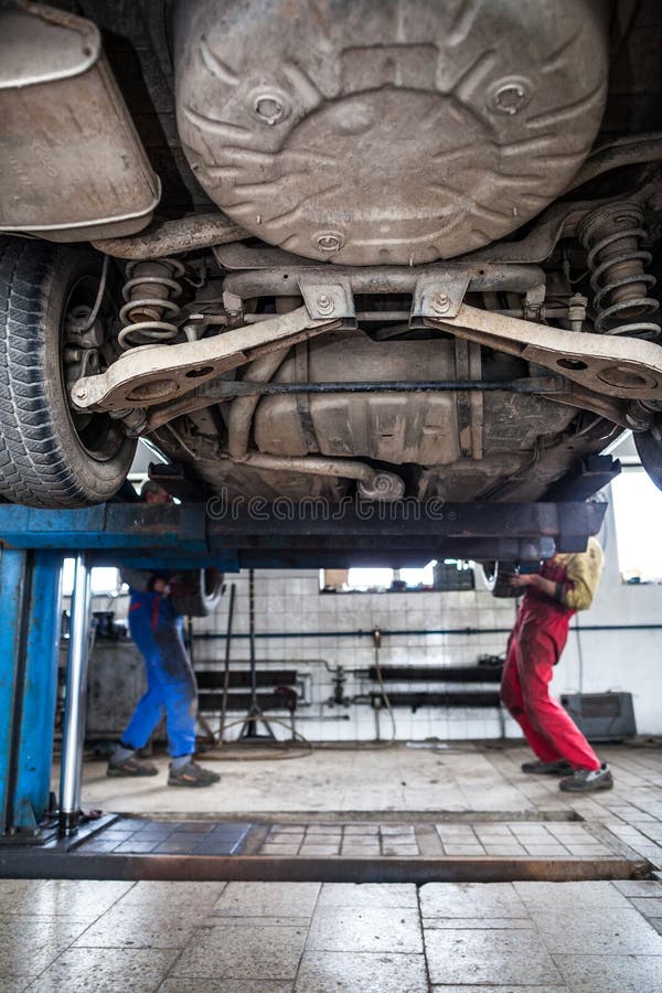Dentro de uma garagem - dois mecânicos que trabalham em um carro fotografia de stock Dentro de uma garagem - dois mecânicos que trabalham em um carro fotografia de stock