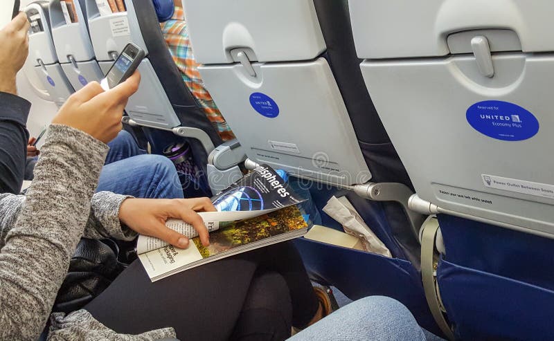 DENVER, Colorado, USA, DECEMBER 30, 2017 - A young woman using United App on her smartphone and holding Hemispheres magazine. Econ stock photo DENVER, Colorado, USA, DECEMBER 30, 2017 - A young woman using United App on her smartphone and holding Hemispheres magazine. Econ stock photo