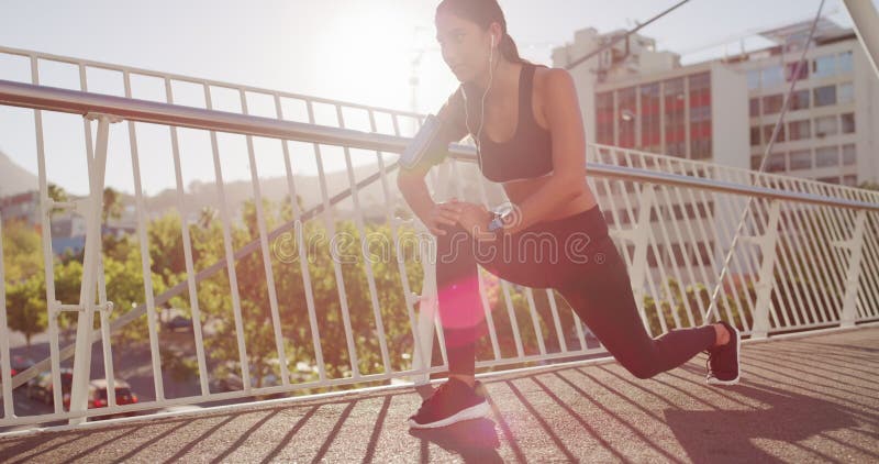 Deportes de salud y ejercicio con la mujer estirando y escuchando música empezando ejercicio físico afuera. mujer joven almacen de metraje de vídeo