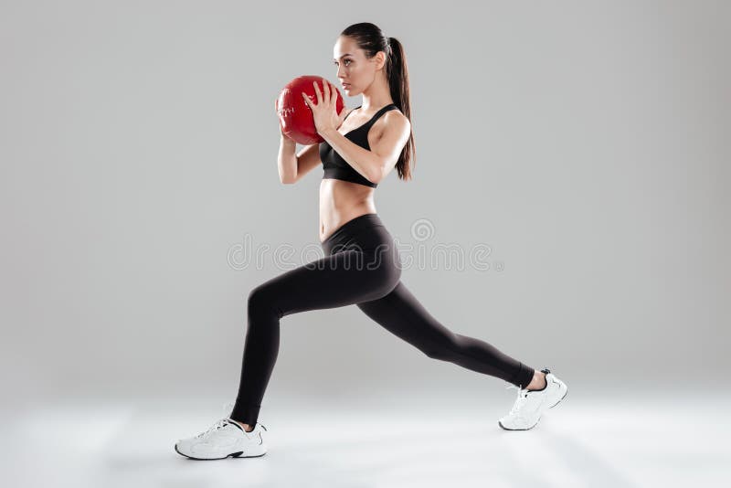 Deportista joven hermosa enfocada que hace ejercicios con la bola de medicina fotografía de archivo Deportista joven hermosa enfocada que hace ejercicios con la bola de medicina fotografía de archivo