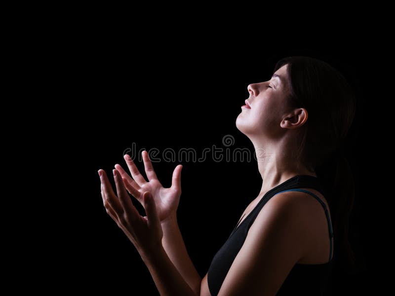 Low key of a faithful woman praying and feeling the presence or being touched by god. Arms outstretched in worship, head up and eyes closed in religious fervor. Black background. Low key of a faithful woman praying and feeling the presence or being touched by god. Arms outstretched in worship, head up and eyes closed in religious fervor. Black background.