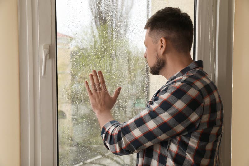 Depressed man looking out window at home