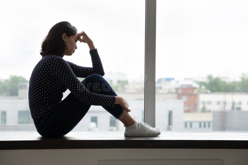 Depressed millennial korean mixed race woman sitting on windowsill crying regretting relations breakup love lost, having problems, suffering from loneliness or feeling insecure alone at home. Depressed millennial korean mixed race woman sitting on windowsill crying regretting relations breakup love lost, having problems, suffering from loneliness or feeling insecure alone at home.